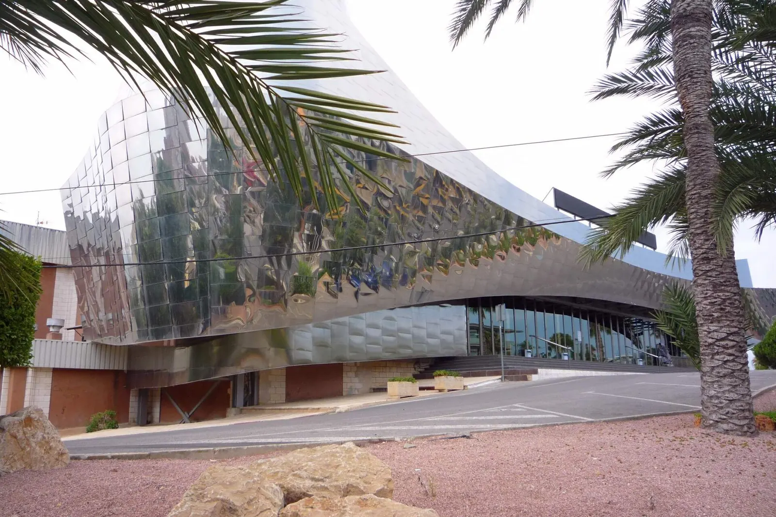 The mirror-bright curve of Benidorm Palace's corner, with palm leaves and a road in front