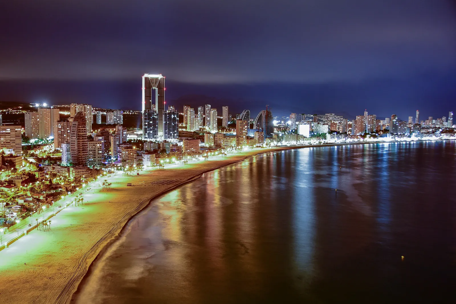 Benidorm's beachfront lit up at night, seen from above, with a tall tower beyond the sand